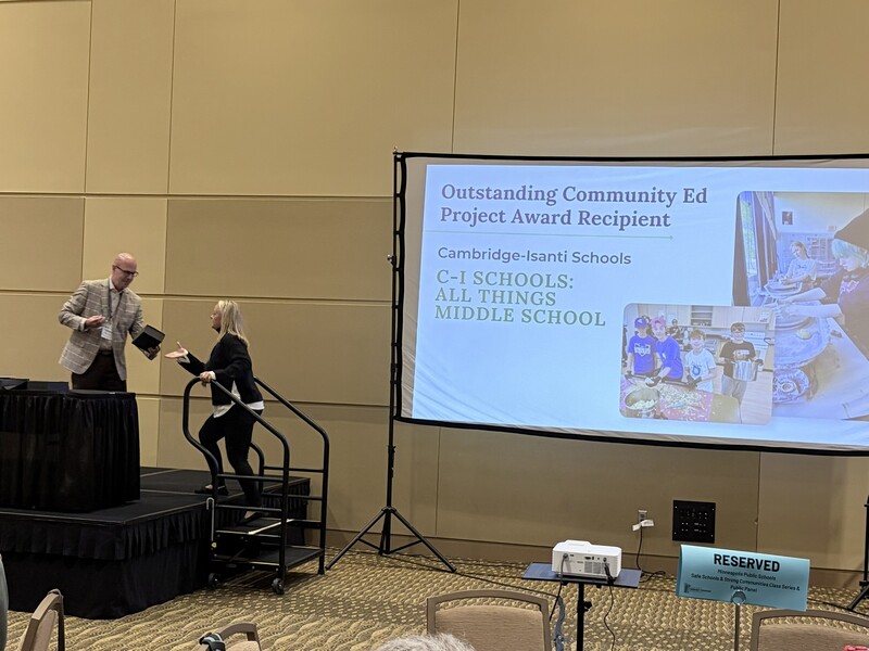 Melissa Lupinek walking onto a stage to receive the Outstanding Community Ed Project Award for Cambridge-Isanti Schools.