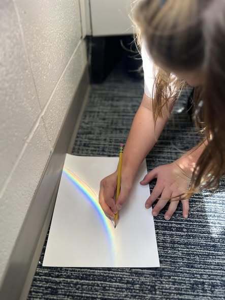 students working on project with rainbow that is coming through window