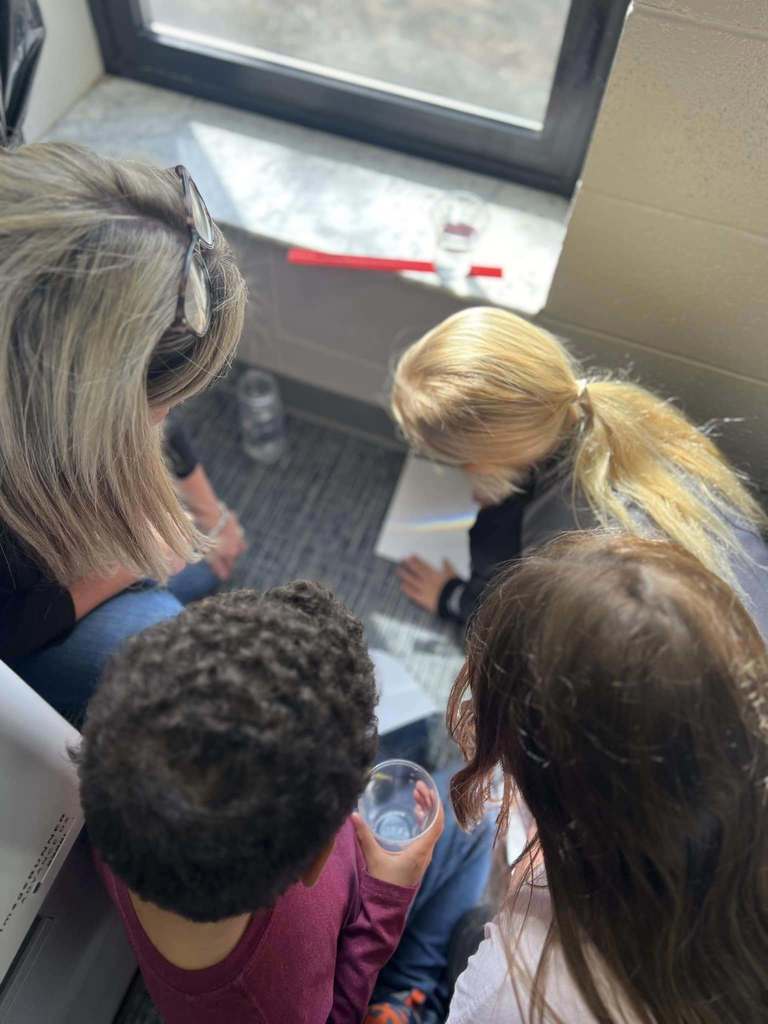 students working on project with rainbow that is coming through window