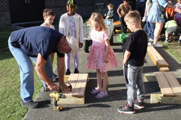 students helping teacher to hammer nails into wood