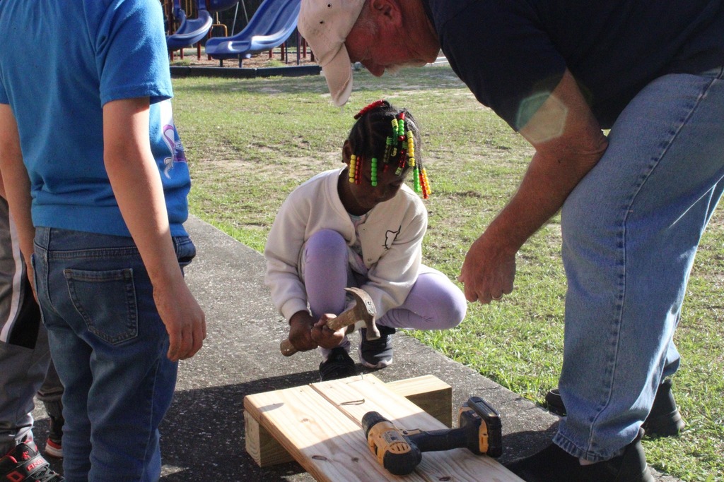 students helping teacher to hammer nails into wood