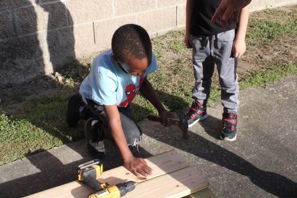 students helping teacher to hammer nails into wood