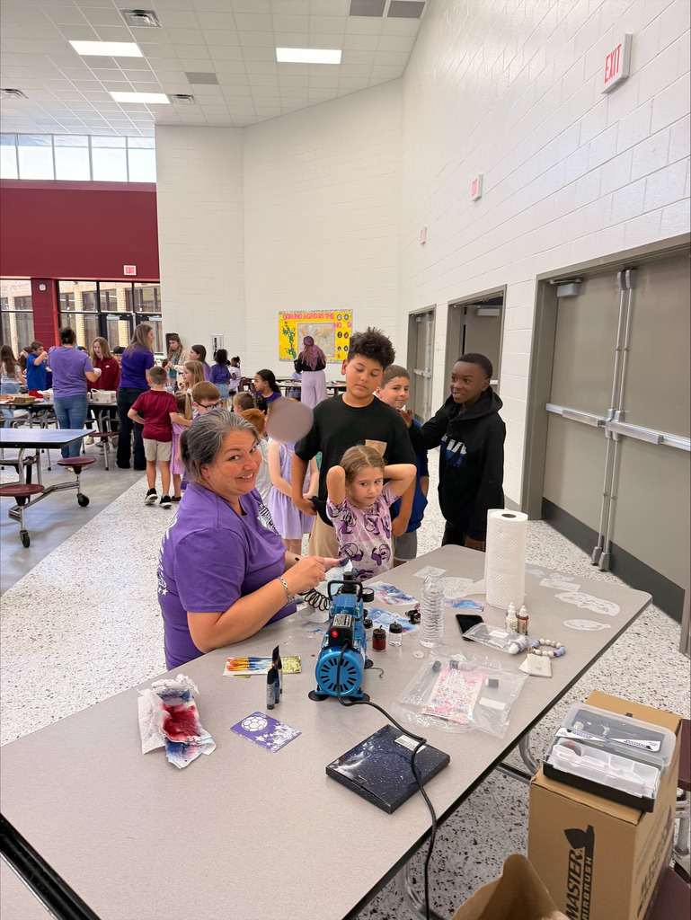 A group of elementary school students at David L. Rainer Elementary celebrate Purple Up Day. Students are wearing purple and participating in activities such as eating pizza and ice cream, getting their faces painted, and enjoying time together. The event honors military children during the Month of the Military Child.