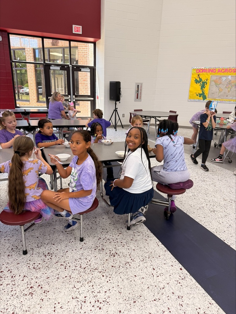 A group of elementary school students at David L. Rainer Elementary celebrate Purple Up Day. Students are wearing purple and participating in activities such as eating pizza and ice cream, getting their faces painted, and enjoying time together. The event honors military children during the Month of the Military Child.