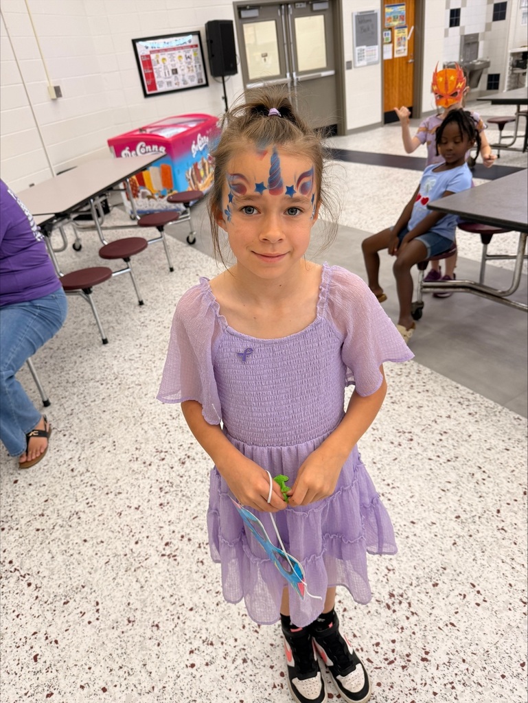 A group of elementary school students at David L. Rainer Elementary celebrate Purple Up Day. Students are wearing purple and participating in activities such as eating pizza and ice cream, getting their faces painted, and enjoying time together. The event honors military children during the Month of the Military Child.