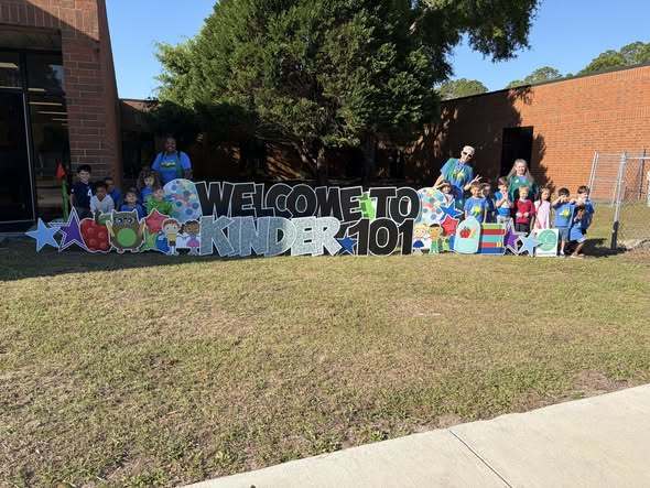 Student and teachers by "welcome to kinder 101" sign