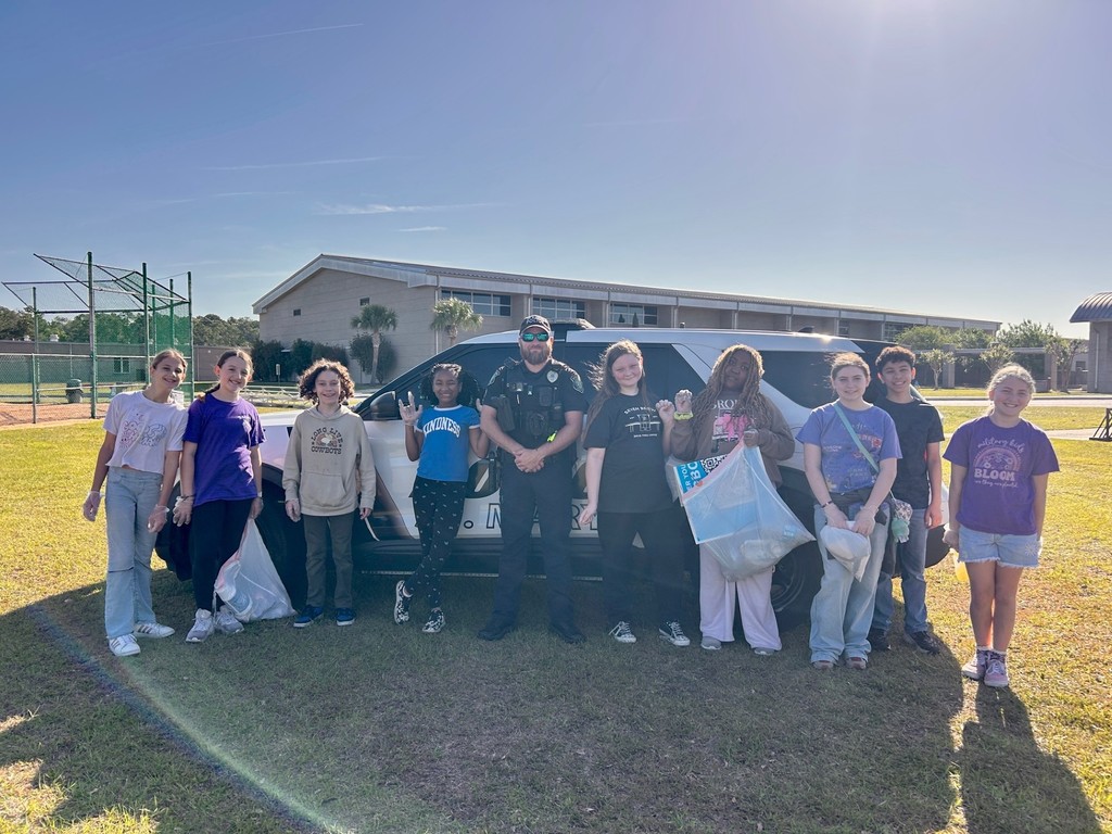Students with SRO in front of police vehicle after picking  up trash.