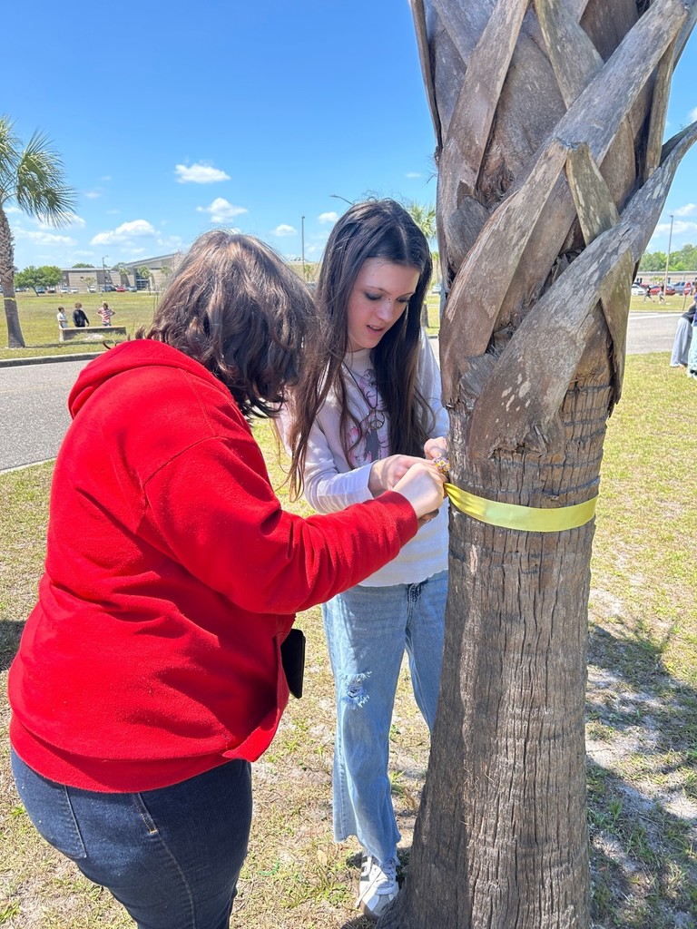Two students tying a yellow ribbon around a tree.