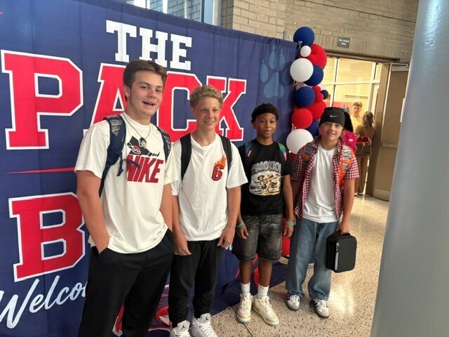 Students in the hallway on the first day of school smiling and waving.