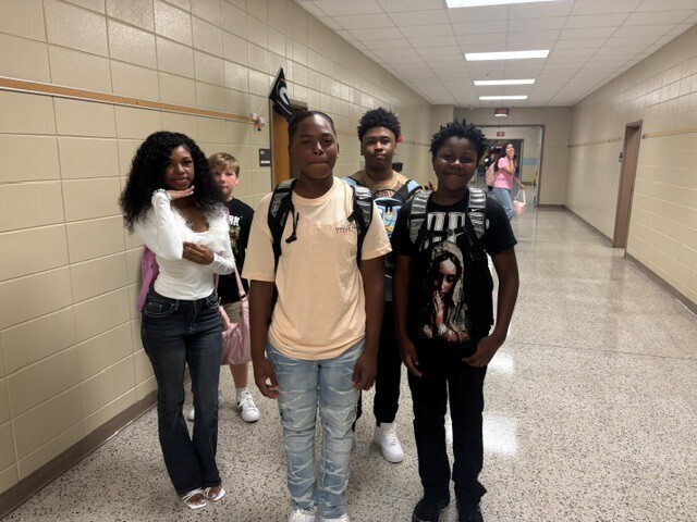 Students in the hallway on the first day of school smiling and waving.