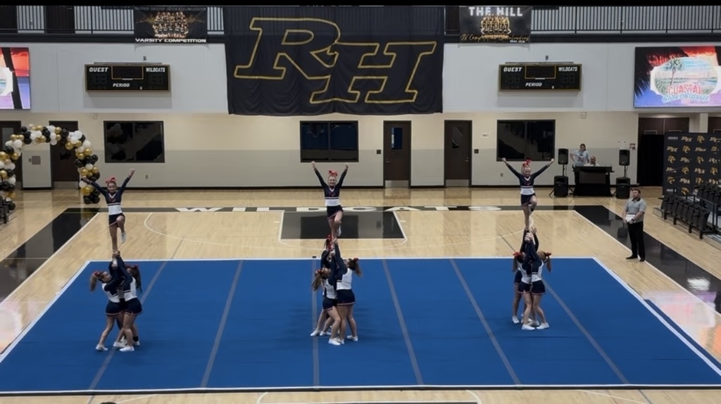 Cheerleaders on the mat competing. Girls being raised above their heads holding a V pose.