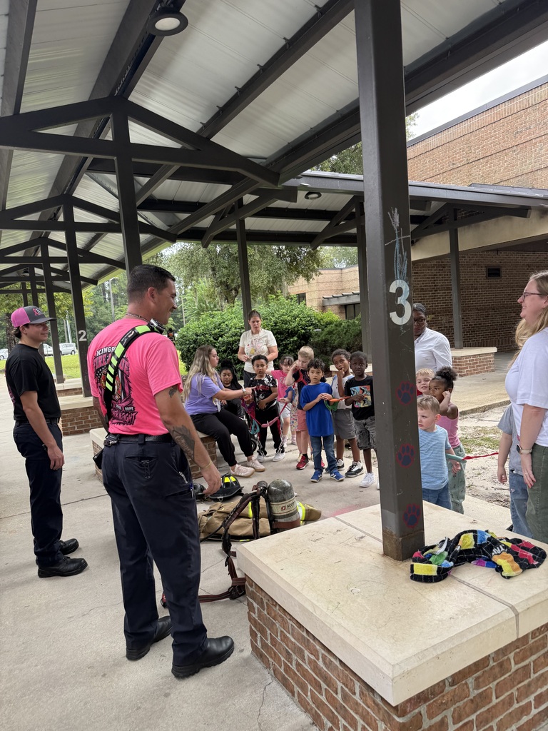 Firefighter talking to students and showing their firefighting gear.