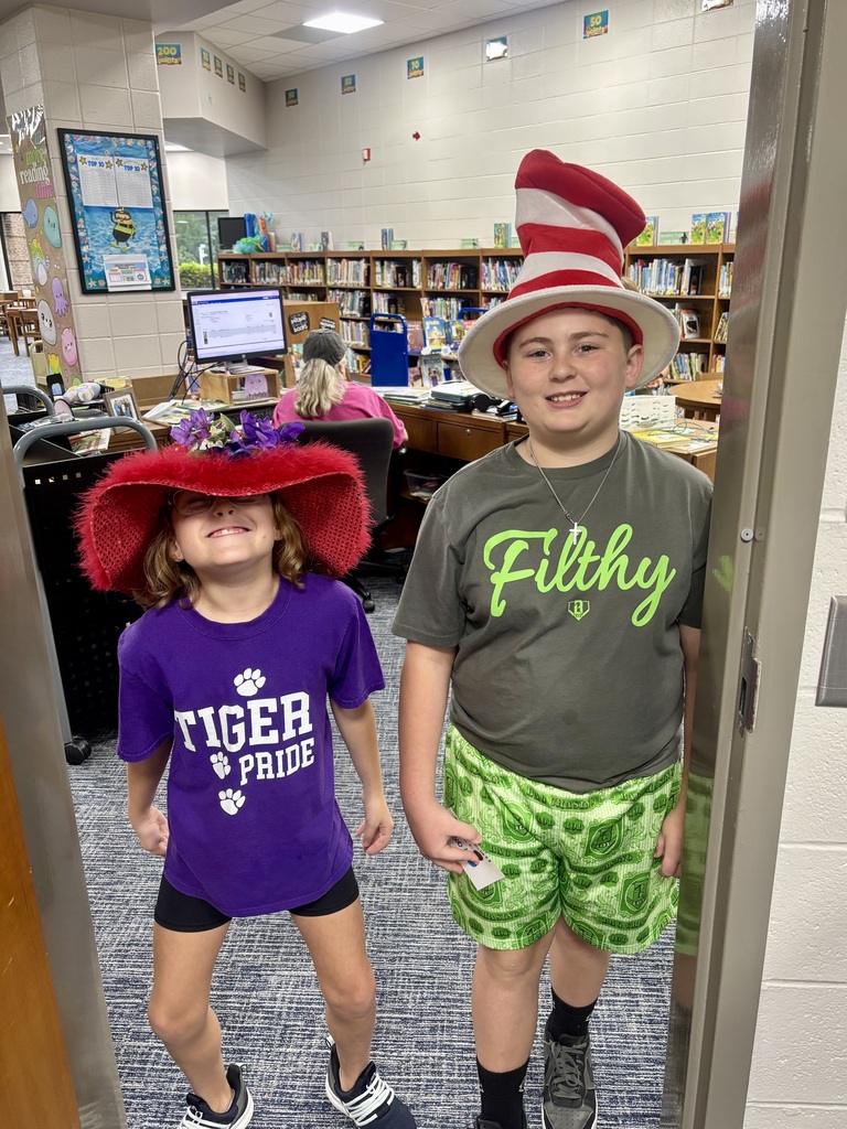 Girl wearing a large red hat and a boy wearing a red and white striped Dr. Seuss-style hat.