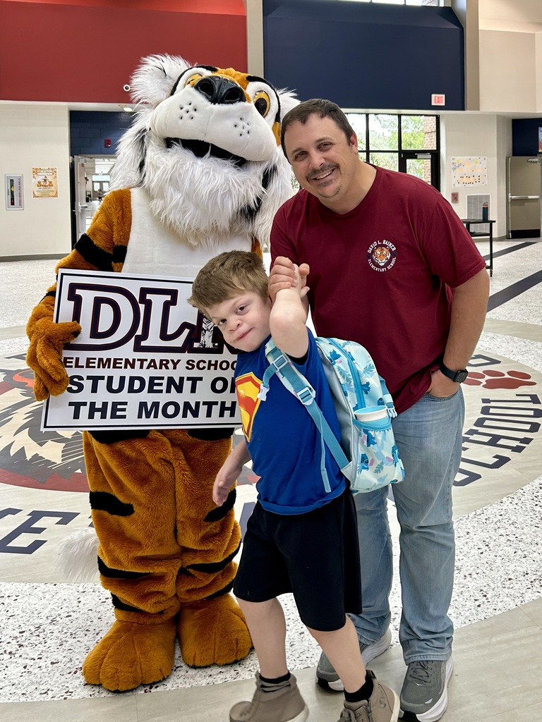 Young boy standing with adult male and Tiger mascot holding a sign that says "DLR Elementary School Student of the Month"