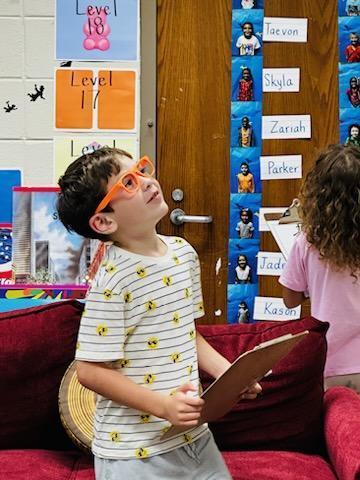Student wearing glasses and writing words they can see in the classroom.
