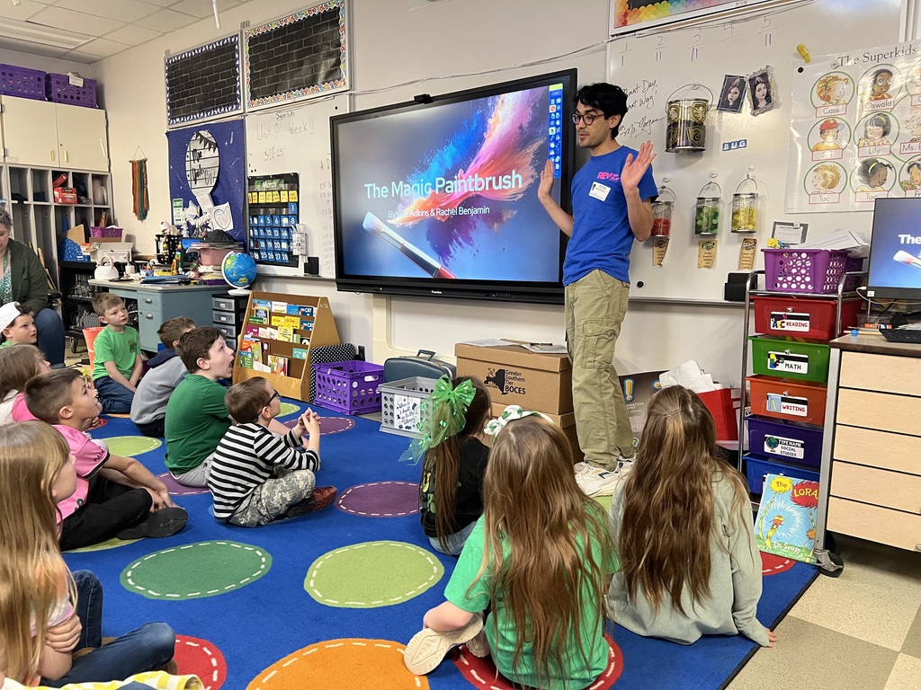 Picture in classroom with students sitting on rug watching a teacher in a blue shirt from Rev theatre