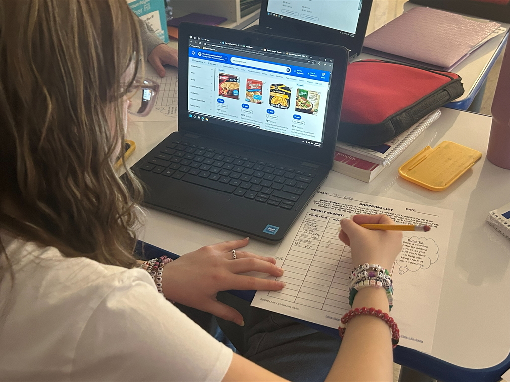 Student writing a budget with lap top in front of them