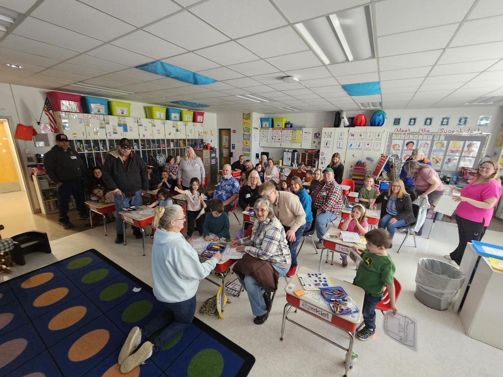 Kindergarten classroom picture with grandparents and thier grandkids sitting together at desks.