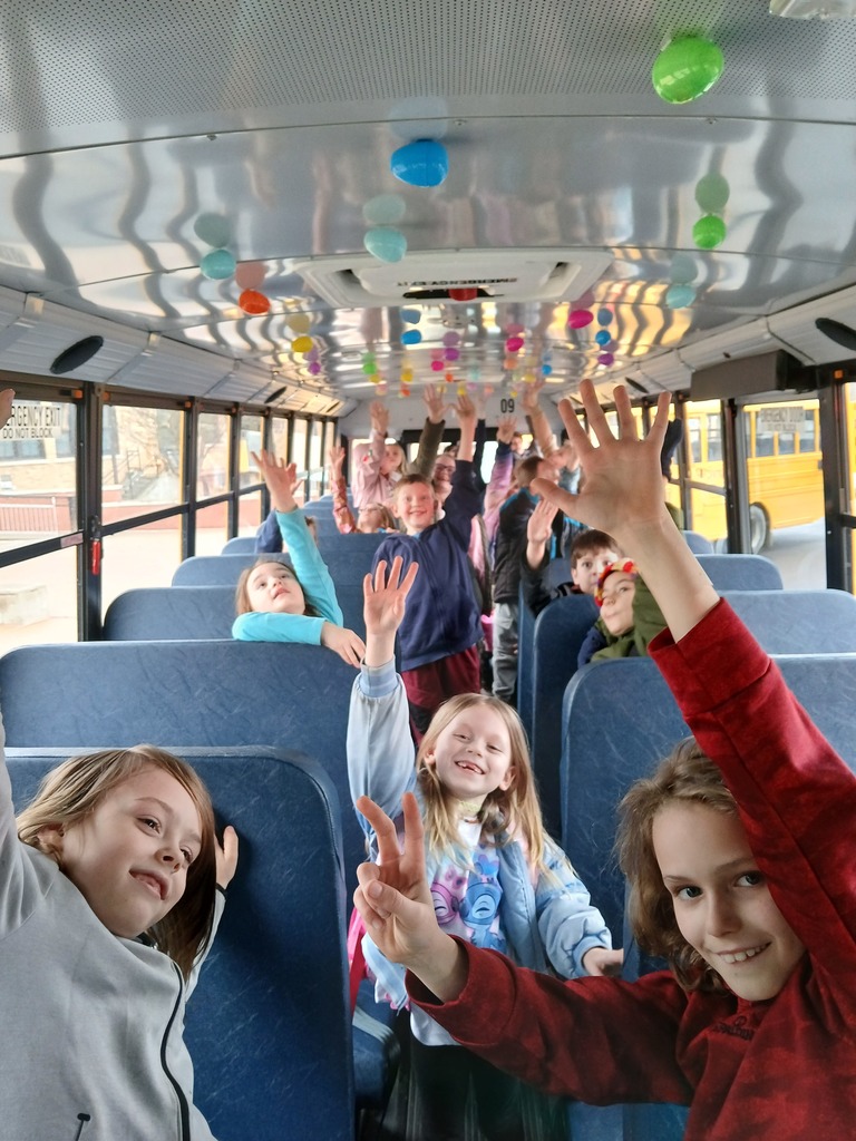 children on bus celebrating an easter egg hunt with hands in the air.