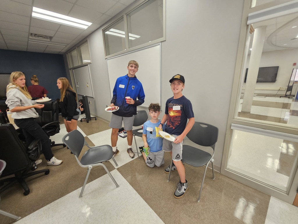 Three students posing and smiling holding paper plates with pizza