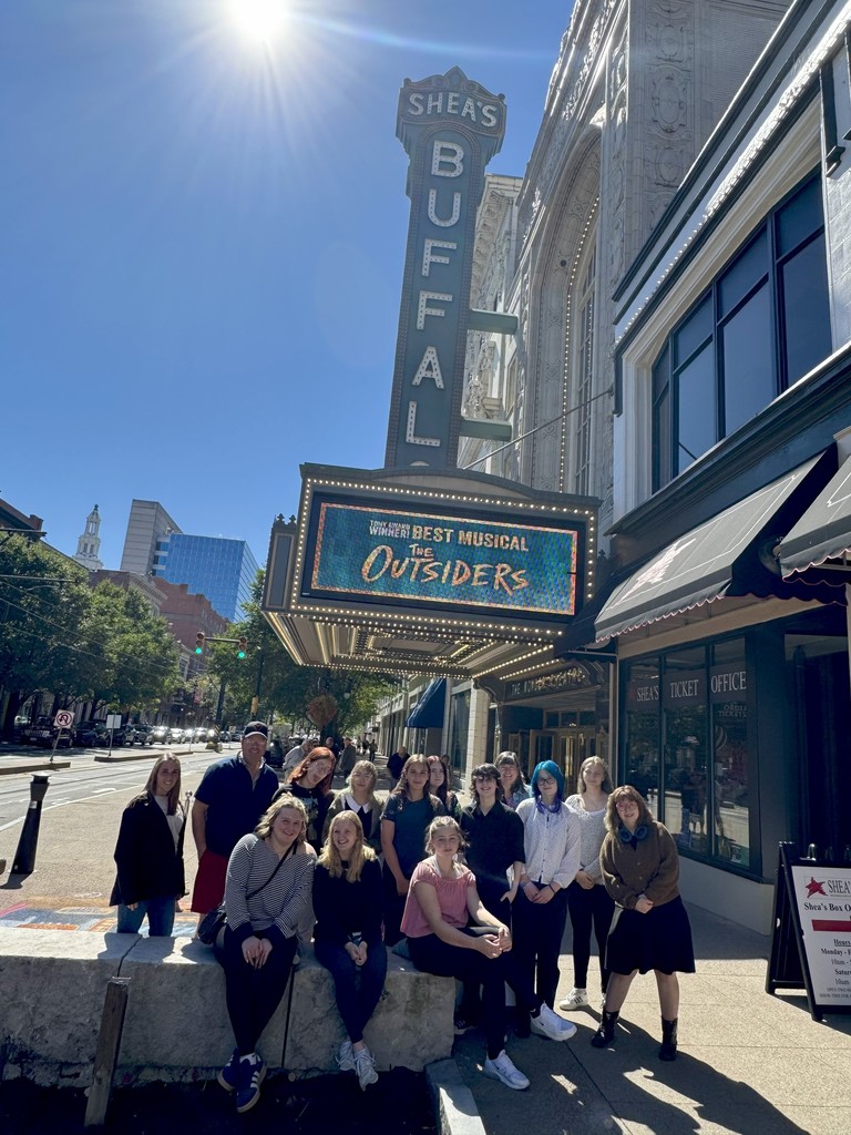 Group picture of students outside in front of Shea's theater with the Outsiders billboard