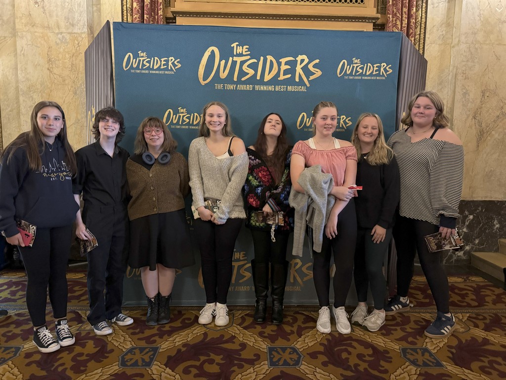 Group picture of students standing in from the of The Outsiders banner