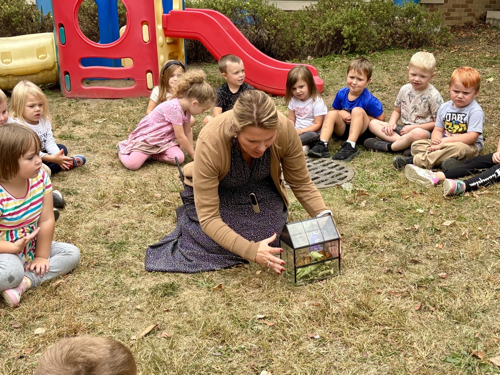 Class sitting around prek teacher as she opens the cage for the monarchbutterfly