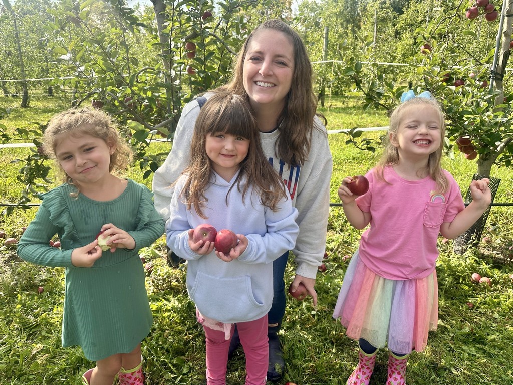 3 students and teacher smiling holding apples