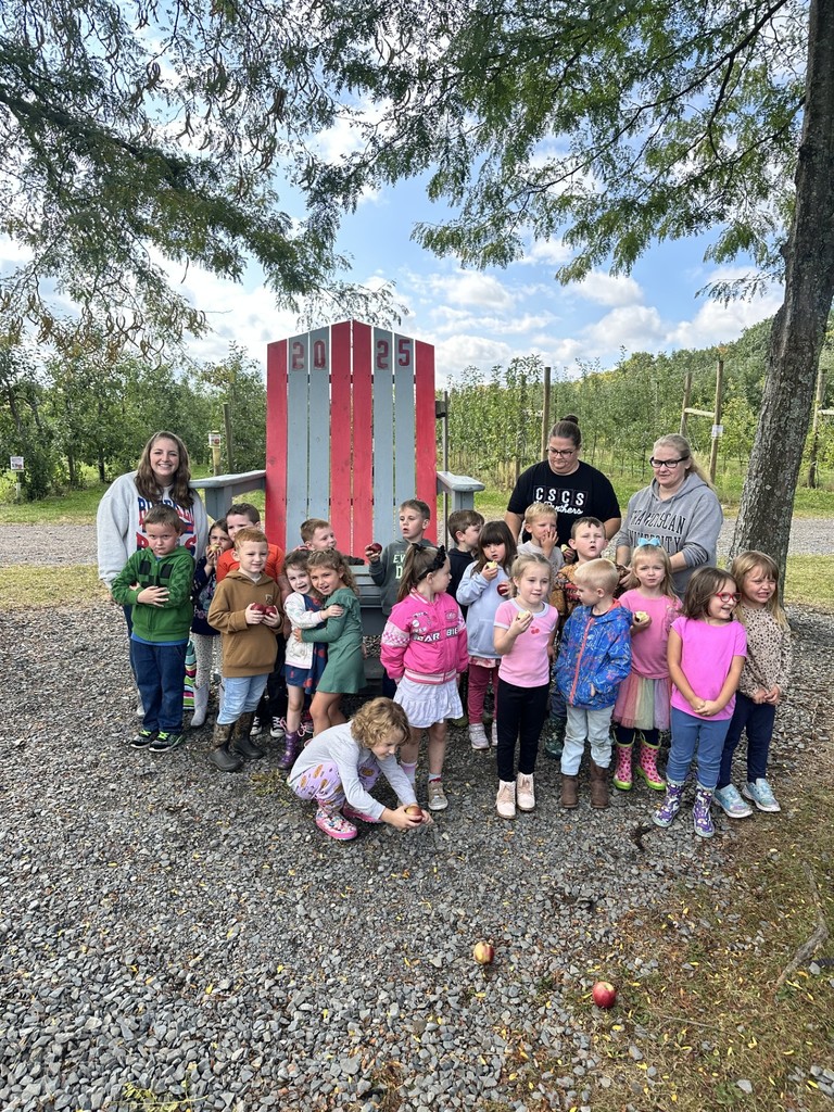 Class of students posing for group picture in front of an oversized wood chair at apple orchard.