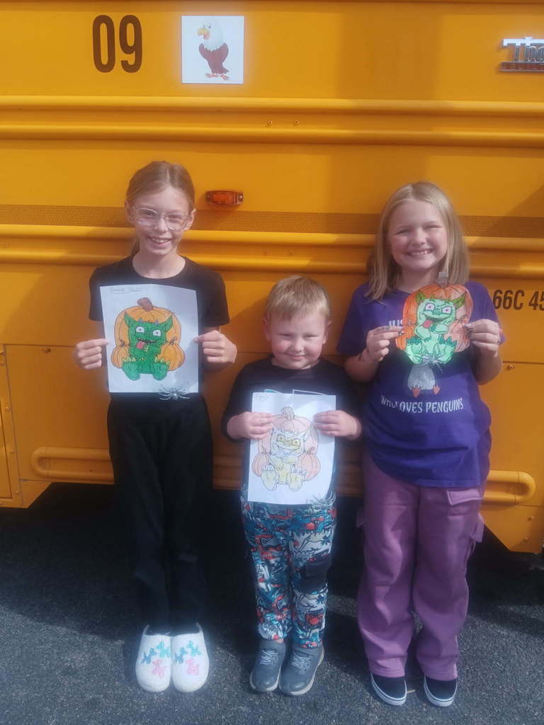 Three elementary students standing in front of bus holding coloring sheets