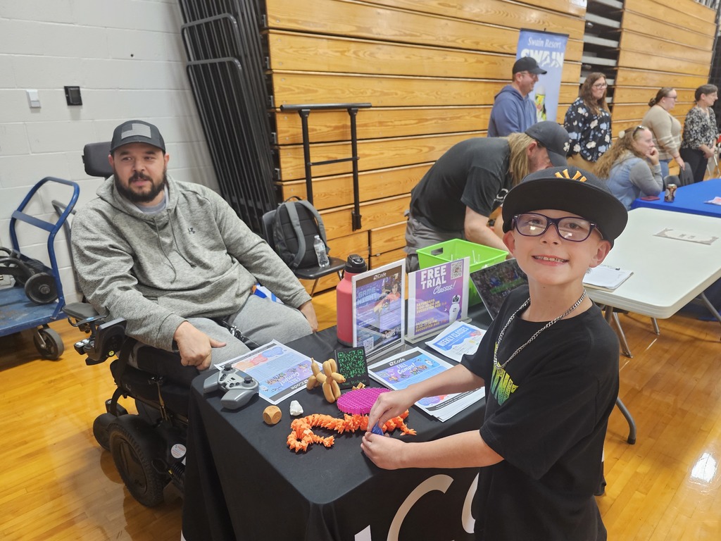 Student smiling with hat at information table during open house.