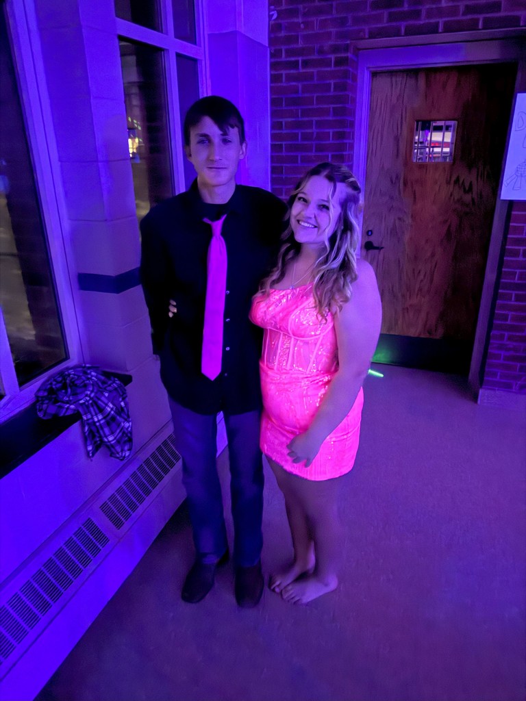 Two students dressed in tie and formal dresses smiling for picture at homecoming dance