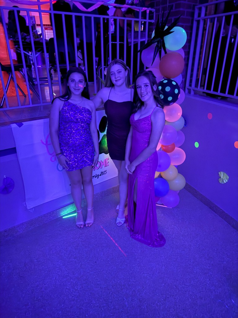 Three students in formal dresses smiling at homecoming dance