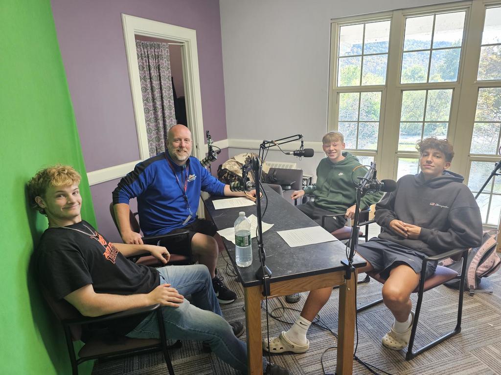 3 students and Athletic Director in front of microphones for podcast
