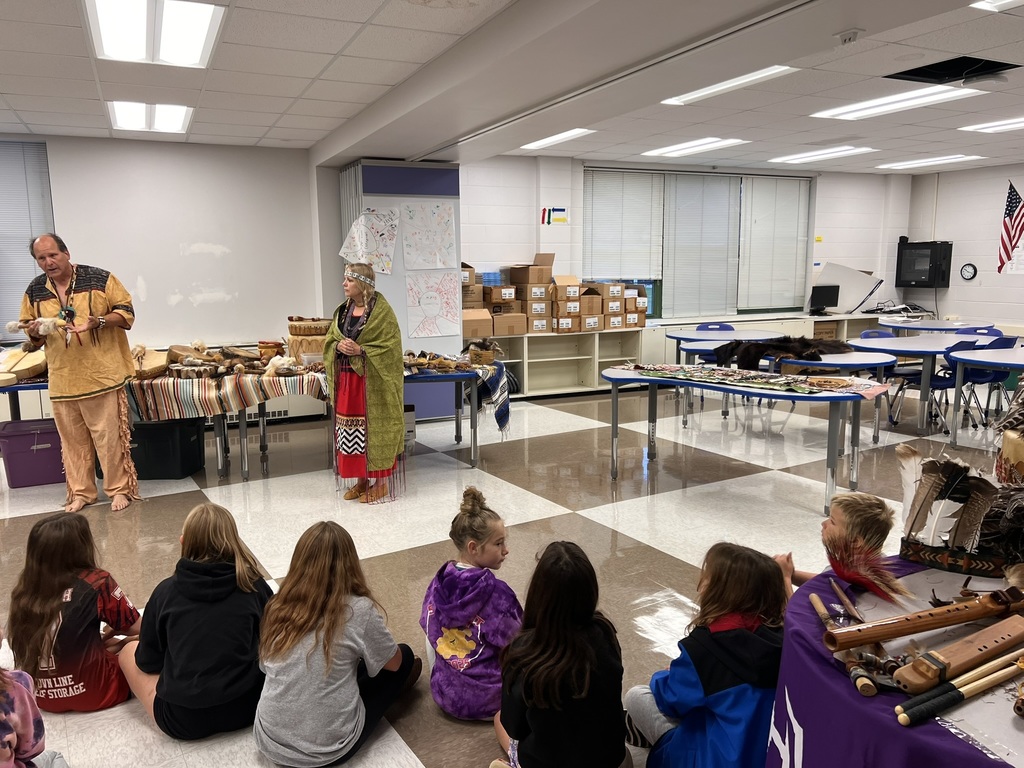 Students sitting on floor watching two presenters dressed in native american clothing.