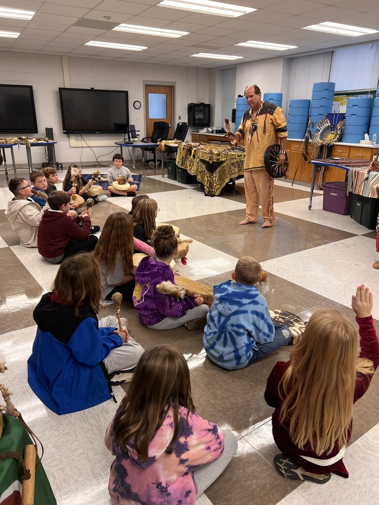Students sitting on the floor  watching a presenter dressed in native american clothing