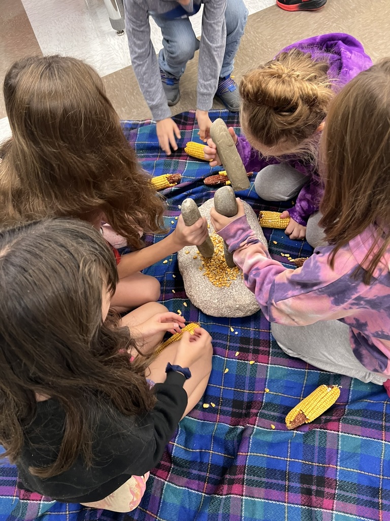 Students sitting on floor using stone to crush maize