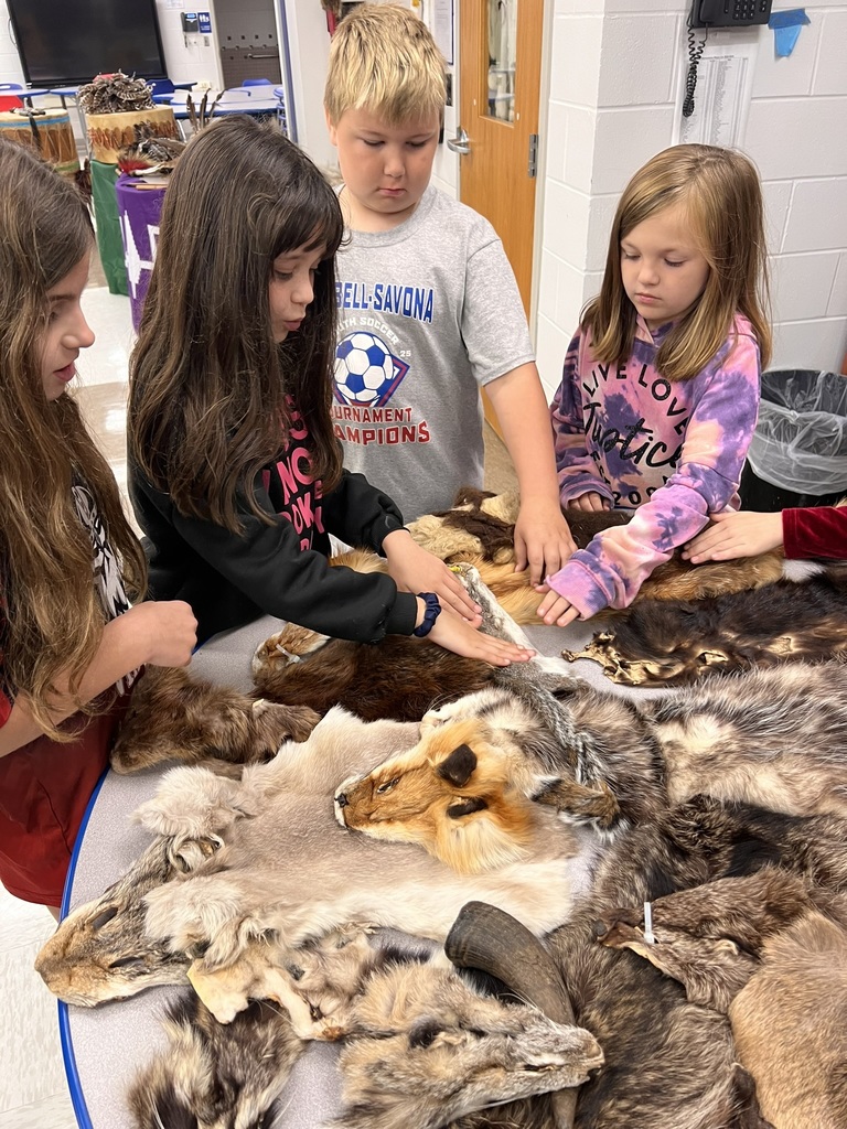 4 students standing around table touching furs