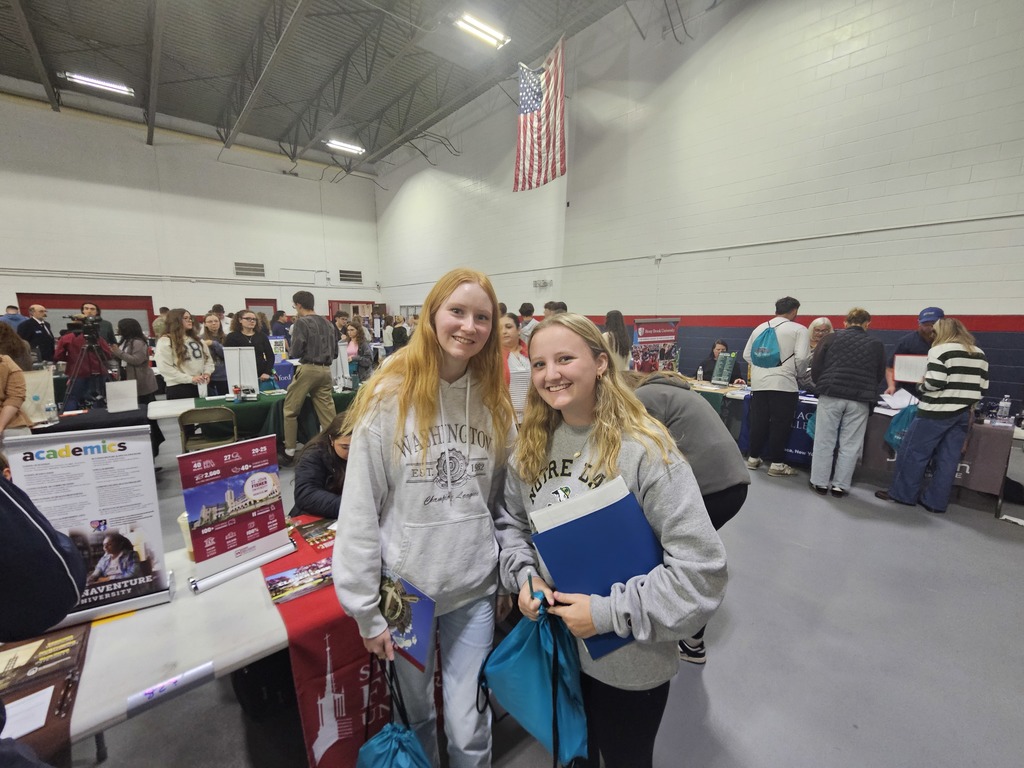 2 students in gray sweatshirts smiling at camera at college fair