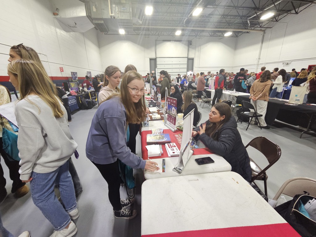 Student with glasses looking at camera while writing notes at college booth