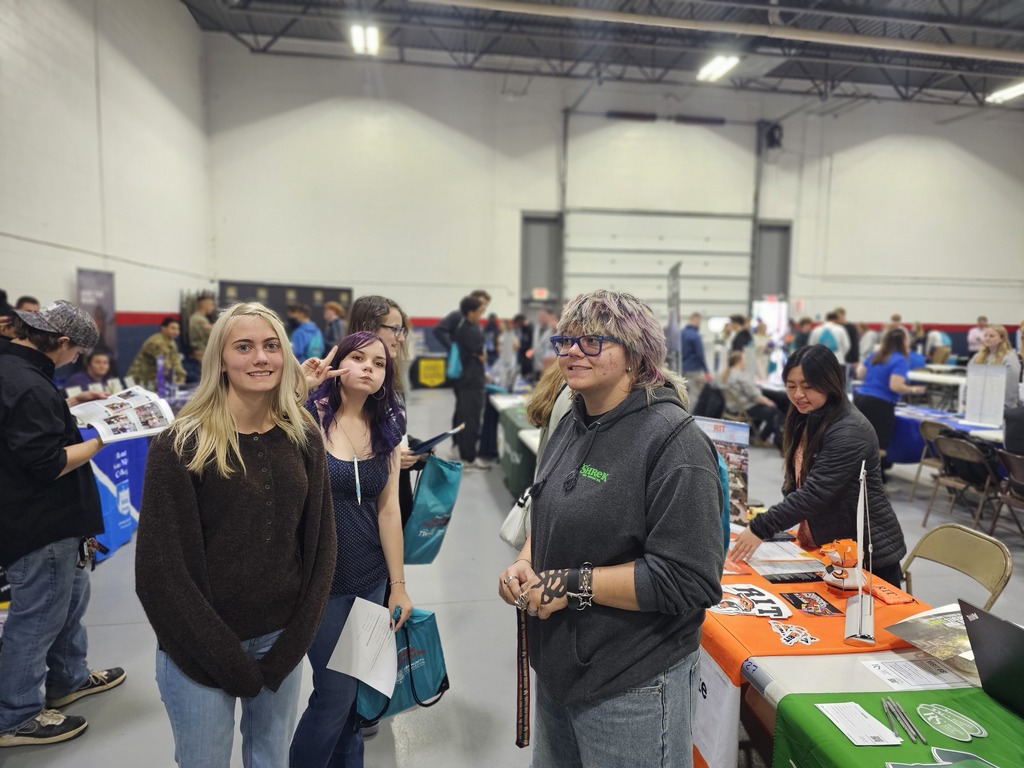 3 students posing for picture in front of college fair information booths