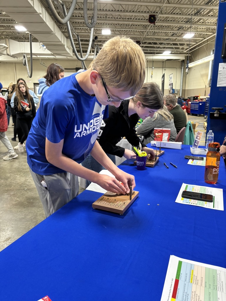 Student in blue shirt and safety glasses leaning over table working on a circuit board