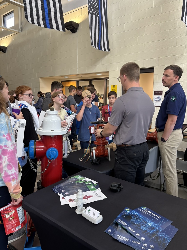 Students gathered around an informational table with adults giving demonstration with firehydrant