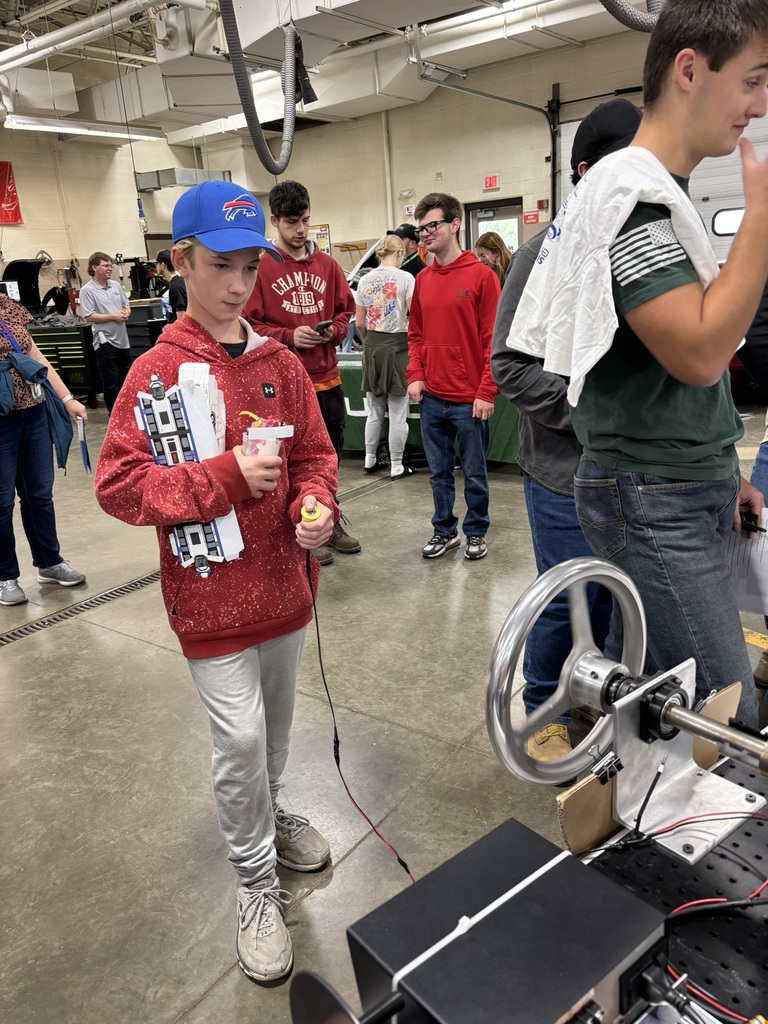 Student in red sweatshirt standing holding a wired button for demonstration