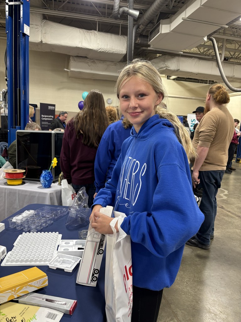 Student in blue Panthers sweatshirt smiling at camera standing at information table
