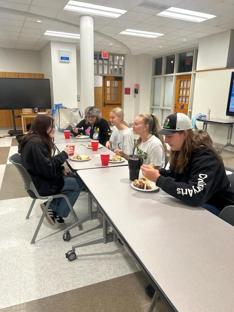 5 students eating breakfast sitting at table.
