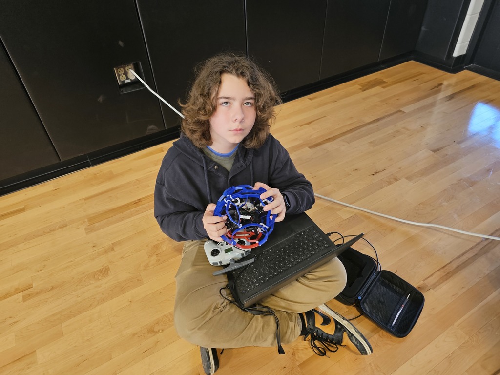 Student sitting on the floor holding drone with computer in his lap.