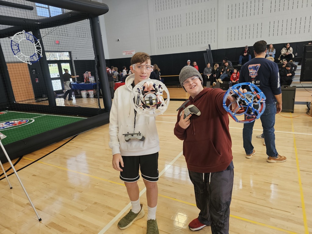 Two students holding drones towards the camera and smiling.