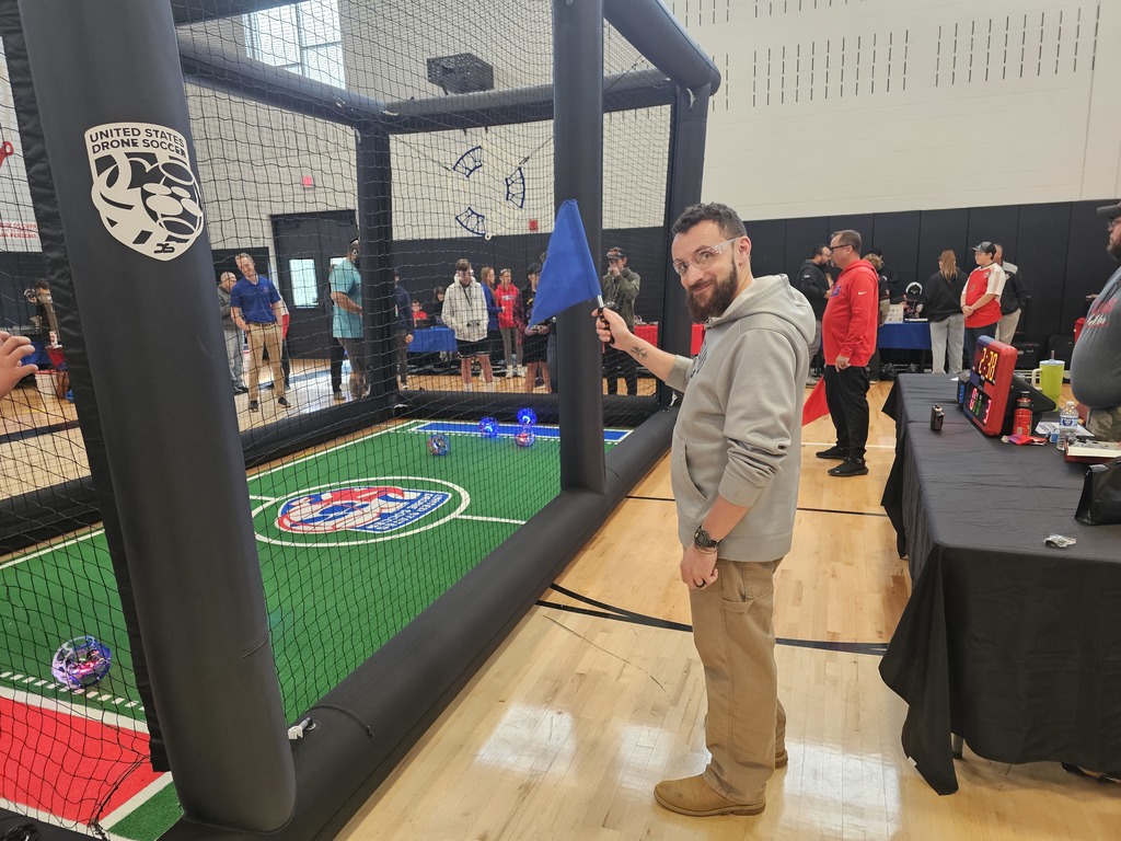 Coach holding a blue flag next to the drone soccer arena