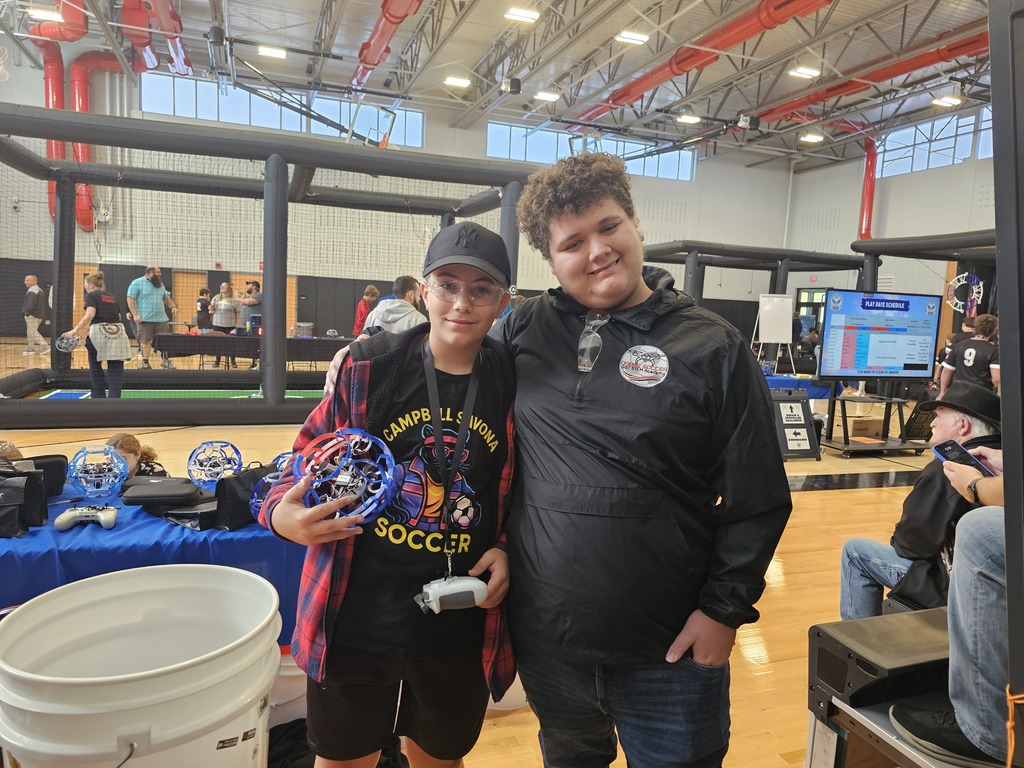 Two students with arms around shoulder posing, one holding a drone.